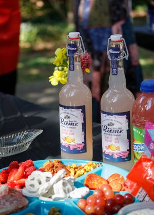 Glass bottles of Lemon Liènte soda arranged on a picnic table with fresh strawberries and assorted snacks and treats.