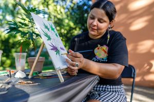 Artist at a table works on a detailed illustration project using drawing tools and art supplies in natural lighting.