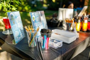Art supplies and markers are arranged on a table outdoors with menus and condiments visible in the background.