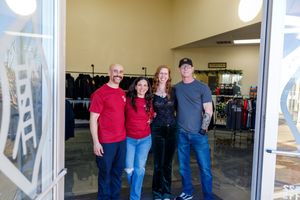 People in casual clothing gather near large glass windows and doors in a retail space.