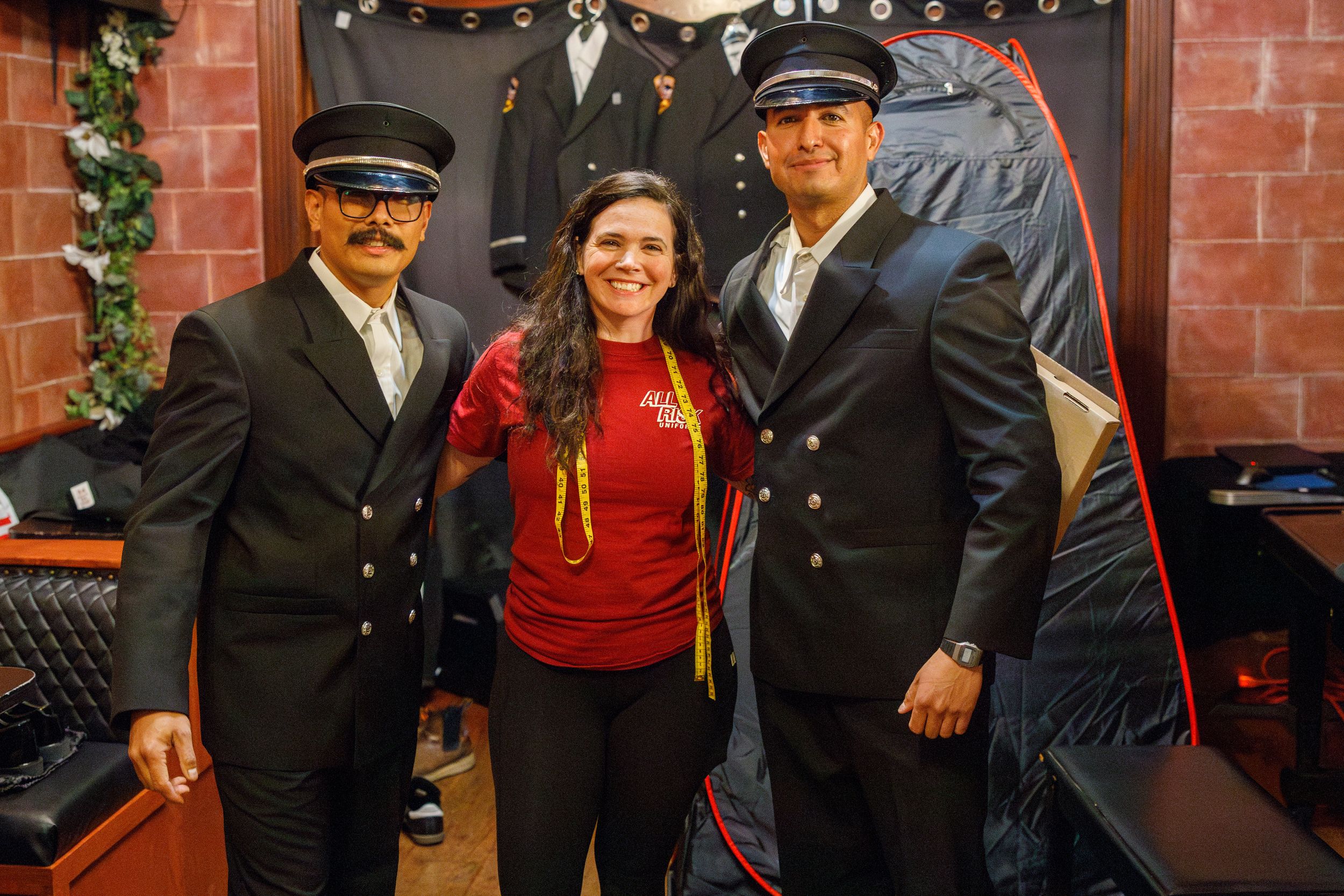 A group poses for photos against a brick wall wearing formal uniforms and casual attire at a gathering.