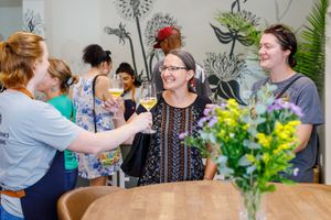 A social gathering with people enjoying drinks around a table with a colorful flower arrangement.