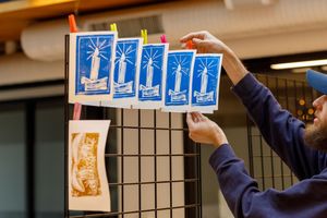 Multiple hands arrange blue paper squares on a black grid display board.