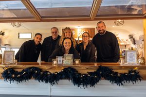 Restaurant staff lineup behind a wooden bar counter decorated with dark blue garlands for the holiday season.