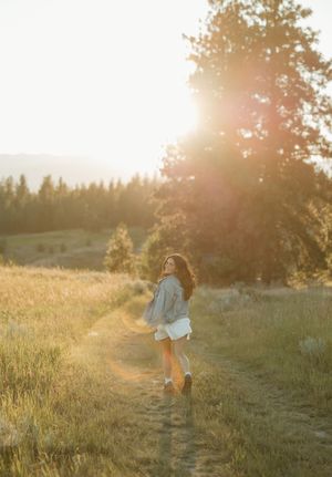A person spins joyfully in a sunlit meadow at golden hour as sunflares illuminate the peaceful summer scene.