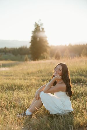 Person in white dress poses gracefully in golden sunlit meadow during sunset photography session.
