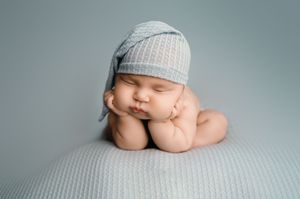 Close-up view of a sleeping baby wearing a white knit cap against a gray background.