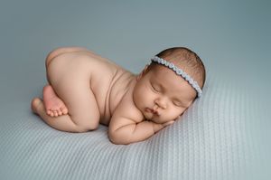A sleeping newborn baby curled up in a peaceful pose on a soft gray textured blanket.