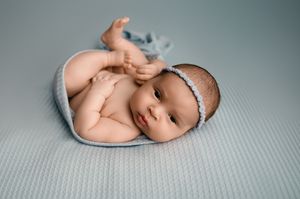 A sweet newborn baby lies curled up on a soft gray blanket in a serene studio setting.
