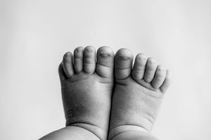 Close-up black and white photograph of tiny newborn baby feet showing delicate toes and wrinkles.