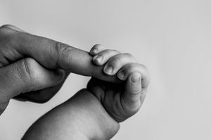 A close-up black and white photo showing a small baby's hand gently holding an adult's finger.