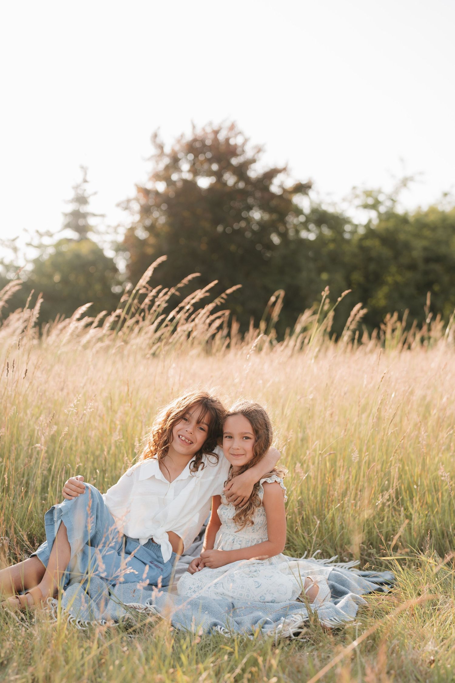 Family members relax on a blanket in a sun-drenched field of tall grass.