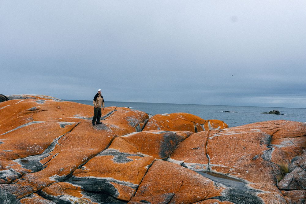 Scenic rocky coastline with orange-colored granite cliffs overlooking a cloudy ocean landscape.