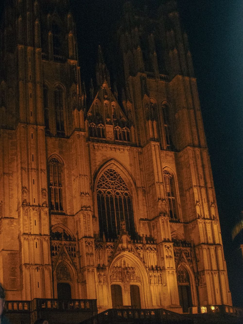 Gothic cathedral facade illuminated at night with ornate arched windows and carved details glowing in warm light.