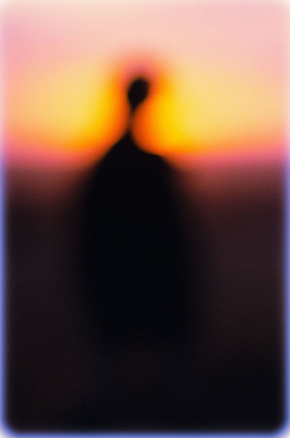 A silhouetted figure stands against a vibrant orange and pink sunset sky creating a dramatic contrast.