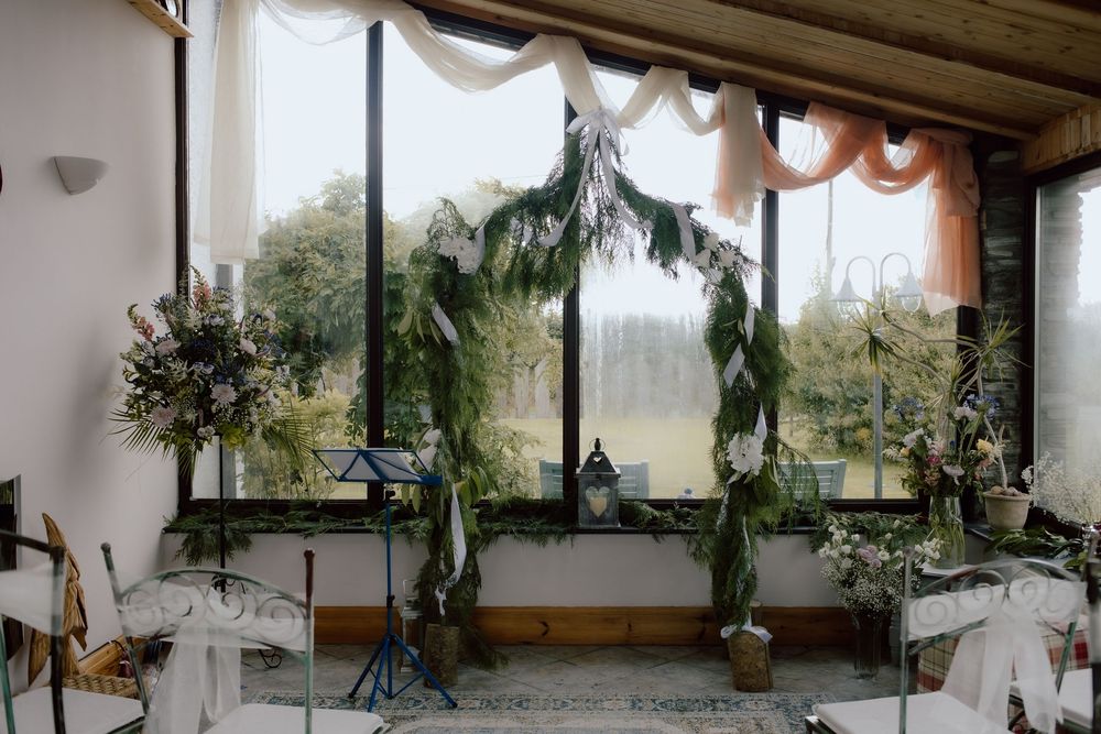 A rustic porch decorated for a wedding with eucalyptus garlands, floral arrangements and white fabric draping.