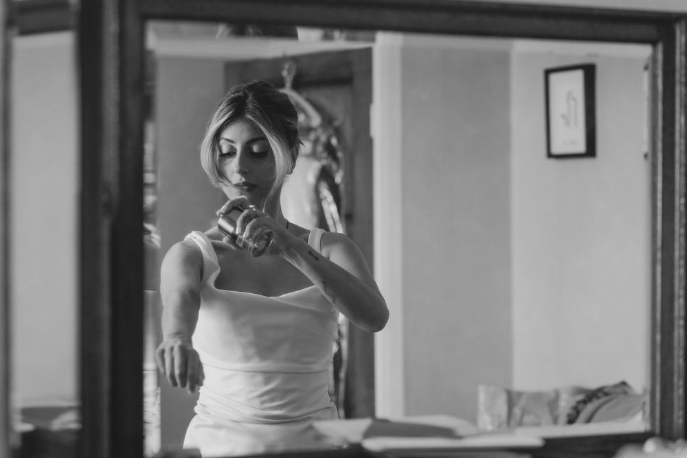 A black and white photograph showing someone taking a mirror selfie while wearing a white sleeveless top.