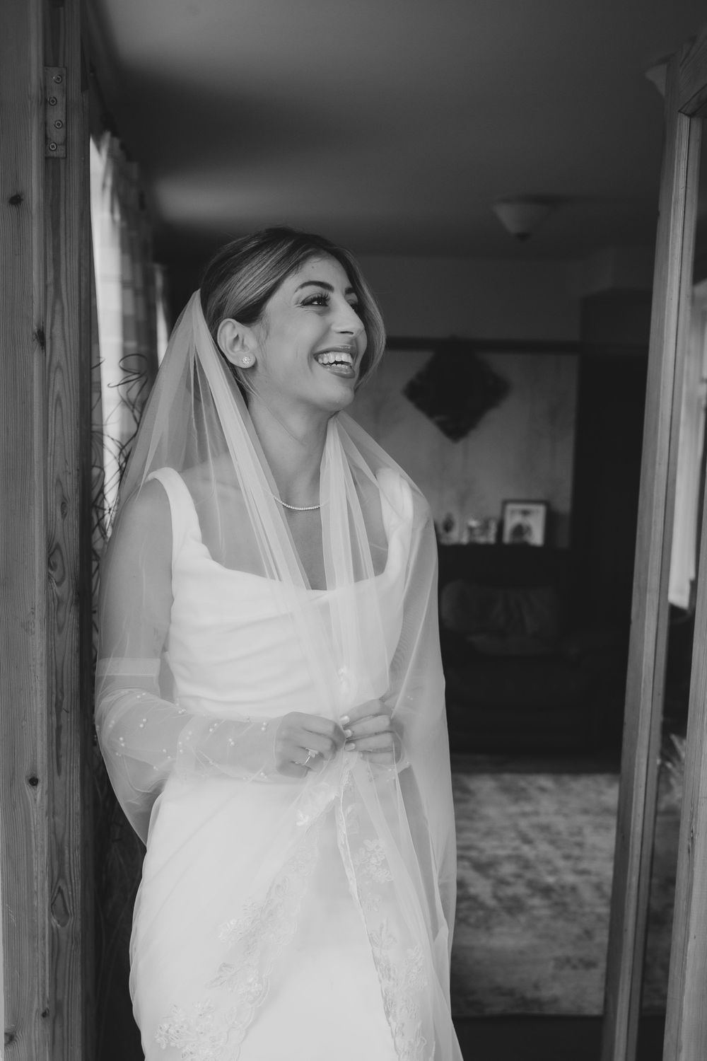 A bride in a white wedding dress and veil smiles joyfully in a black and white portrait.