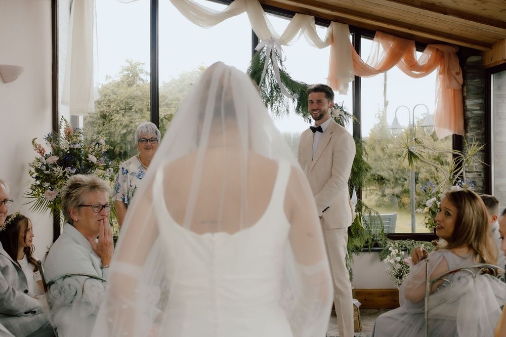 Wedding ceremony taking place in a sunlit gazebo with white draping and floral decorations.