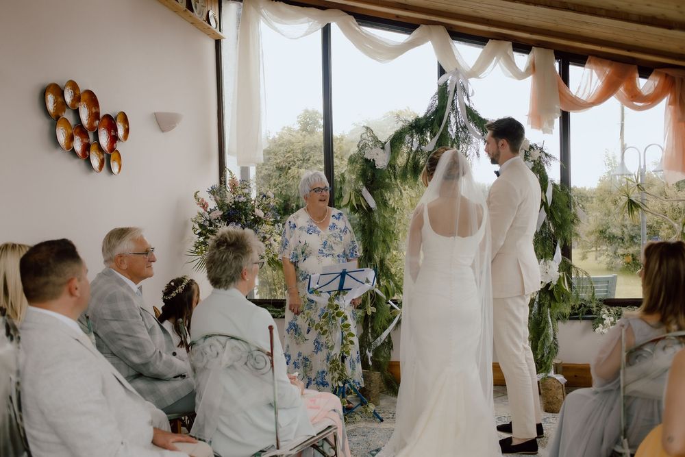 A group of wedding party members in gray suits and white gowns gather together for photos during a wedding reception.
