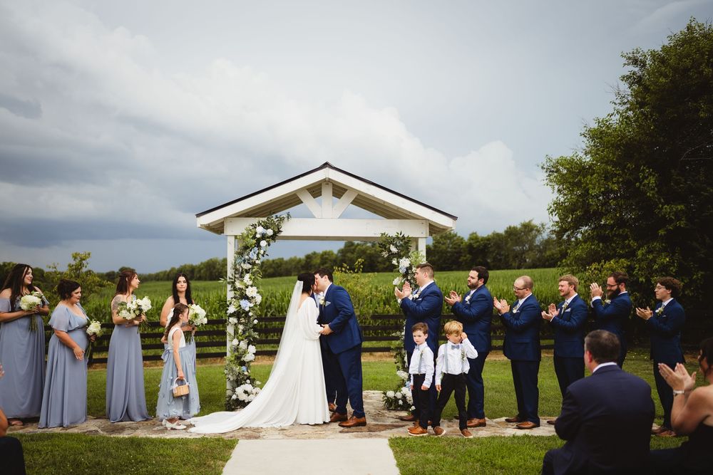 Wedding ceremony in progress at an outdoor venue with white gazebo and rolling hills in the background.