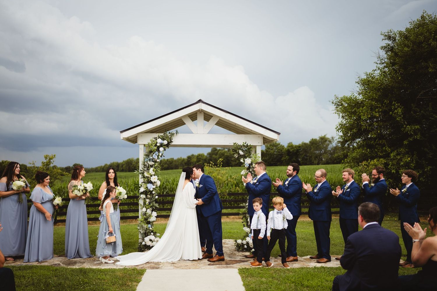 Wedding ceremony in progress at an outdoor venue with white gazebo and rolling hills in the background.