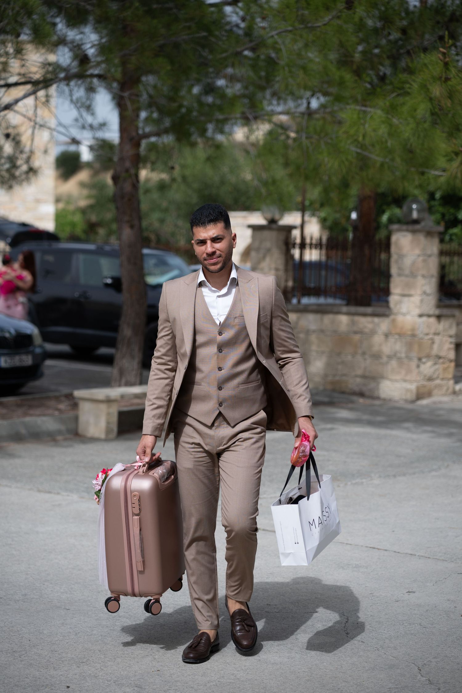 Well-dressed person carrying luggage and shopping bags while walking outdoors.
