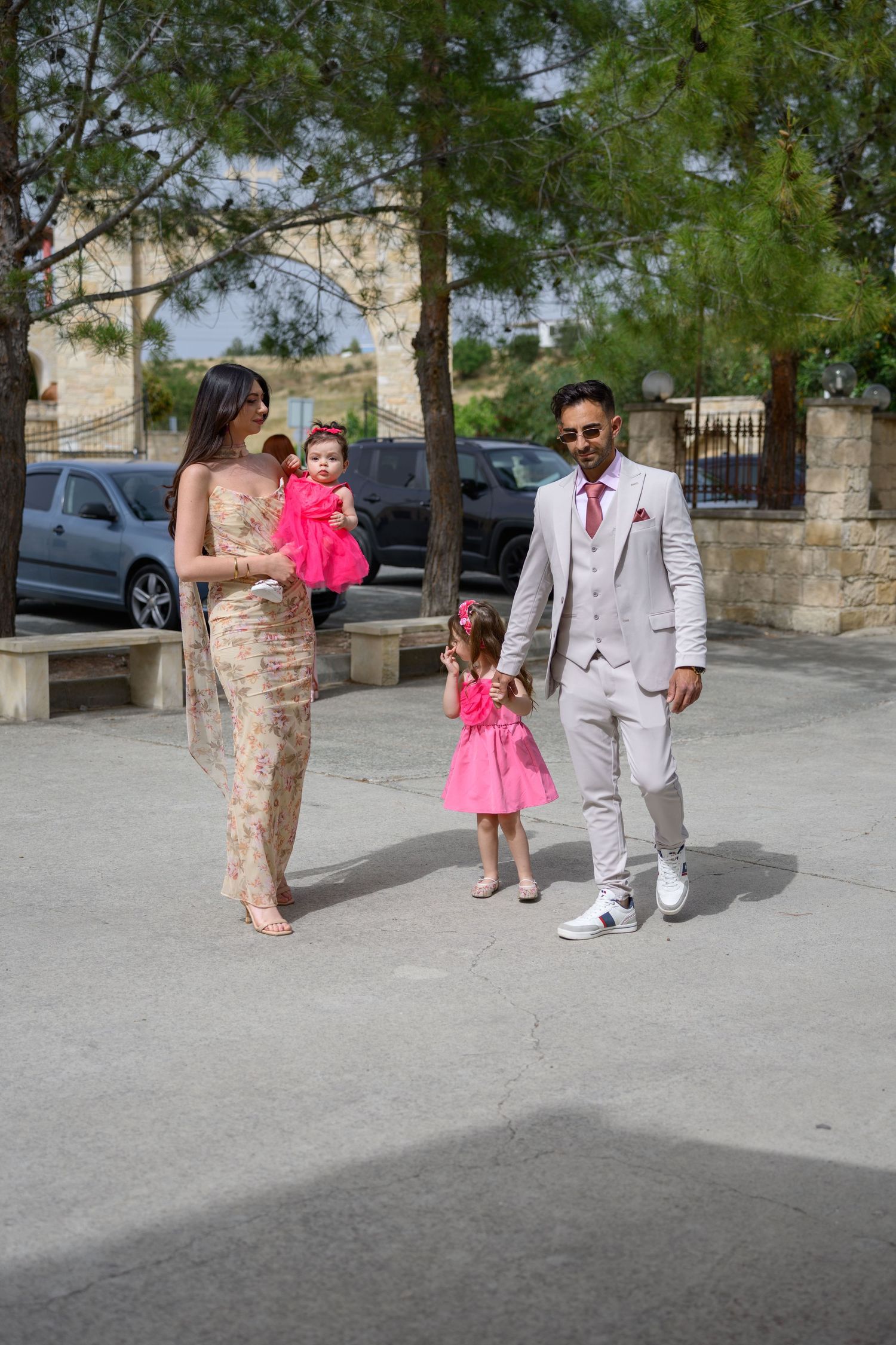 Elegantly dressed family with children in pink dresses walking together outdoors on a sunny day.