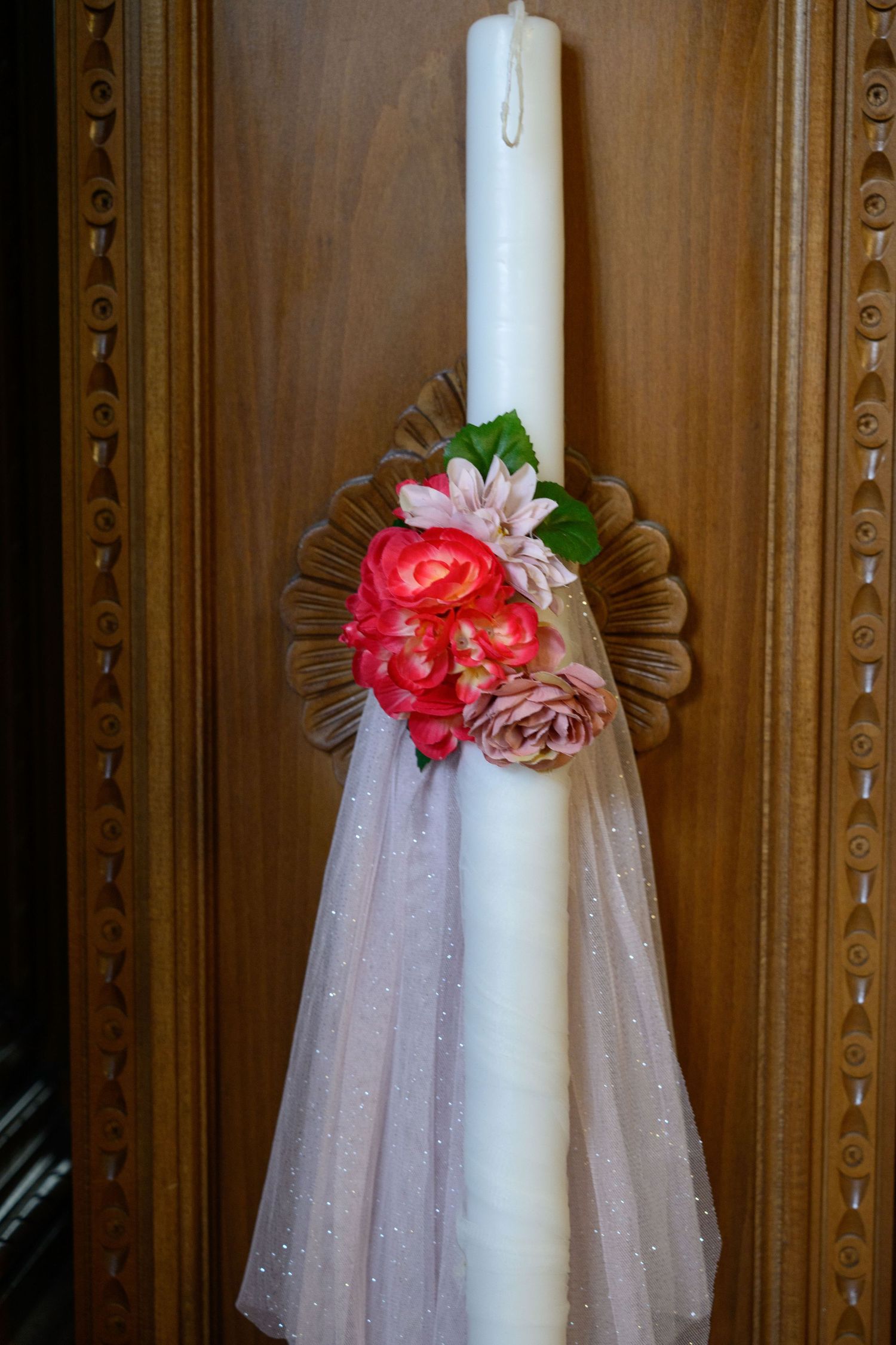 White baptismal candle decorated with pink roses and flowing tulle fabric.