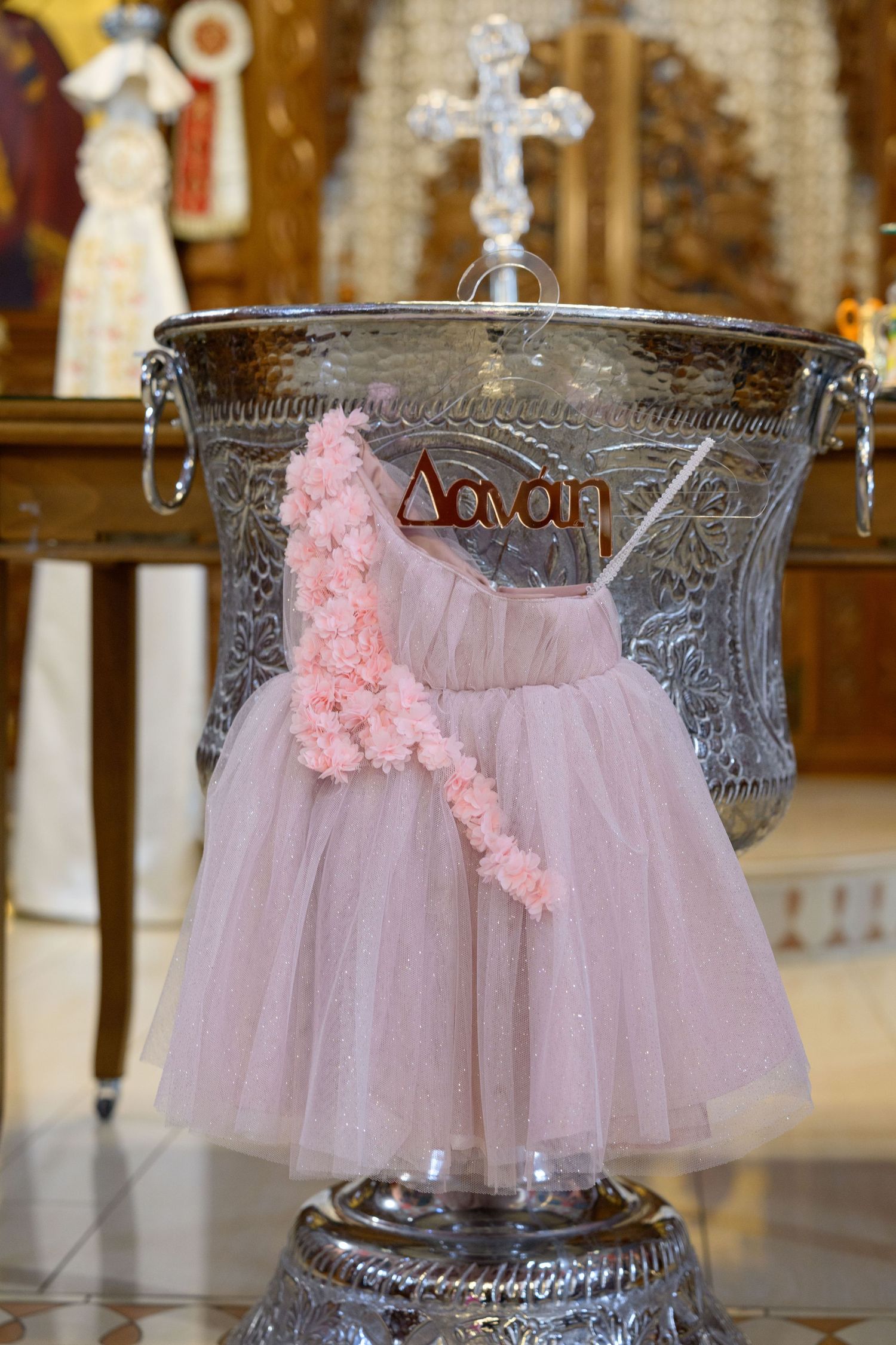 Pink tulle baptism dress displayed on an ornate silver font with a cross on top.