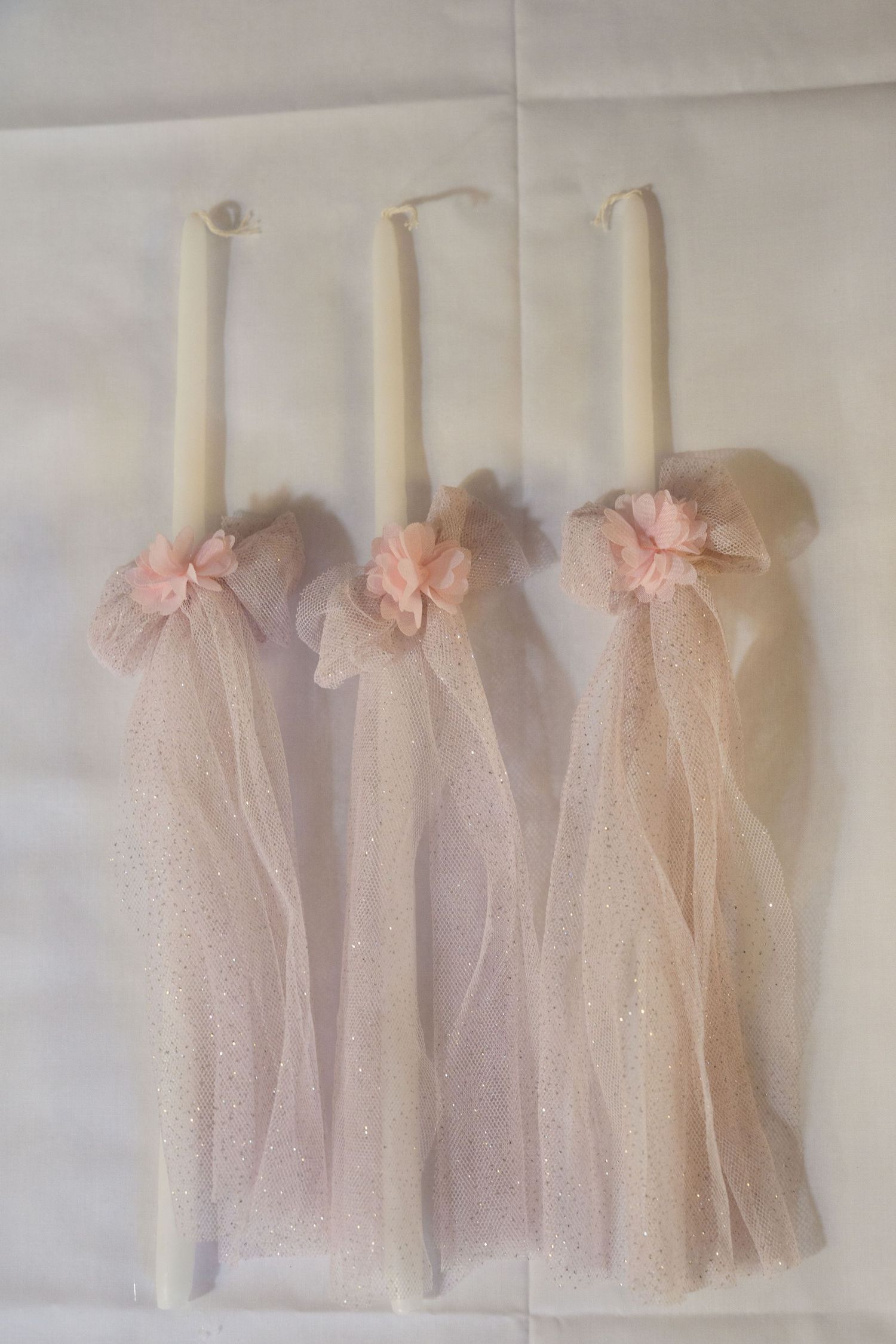 Three white candles decorated with pink tulle bows and veils.