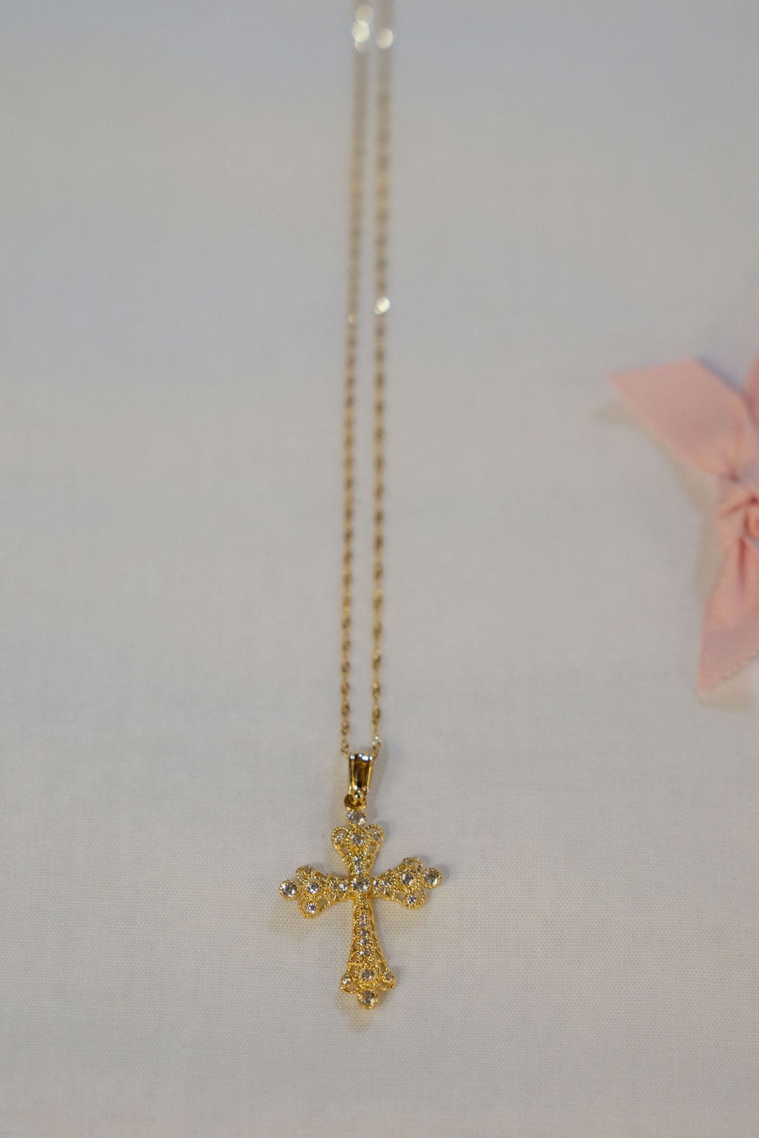 A delicate gold filigree cross pendant necklace on a thin chain against a light background.