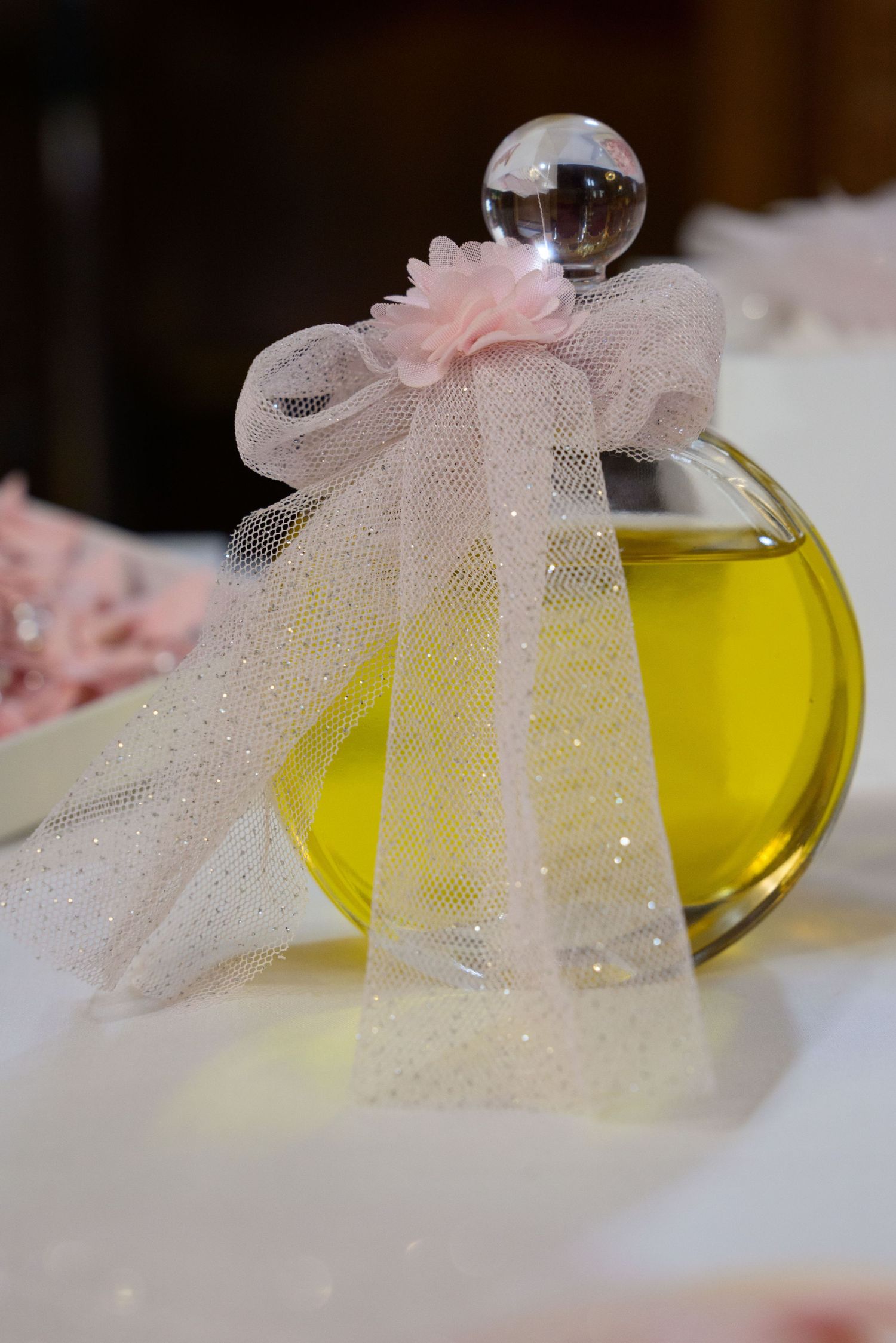 Glass perfume bottle with pink tulle bow and yellow liquid inside.