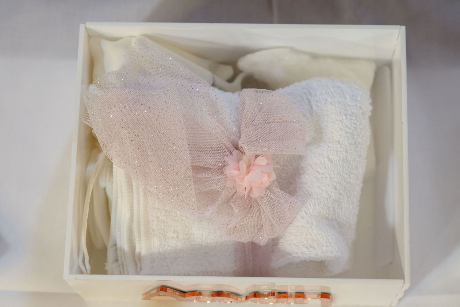 White box containing delicate fabric with pink tulle bow decoration.