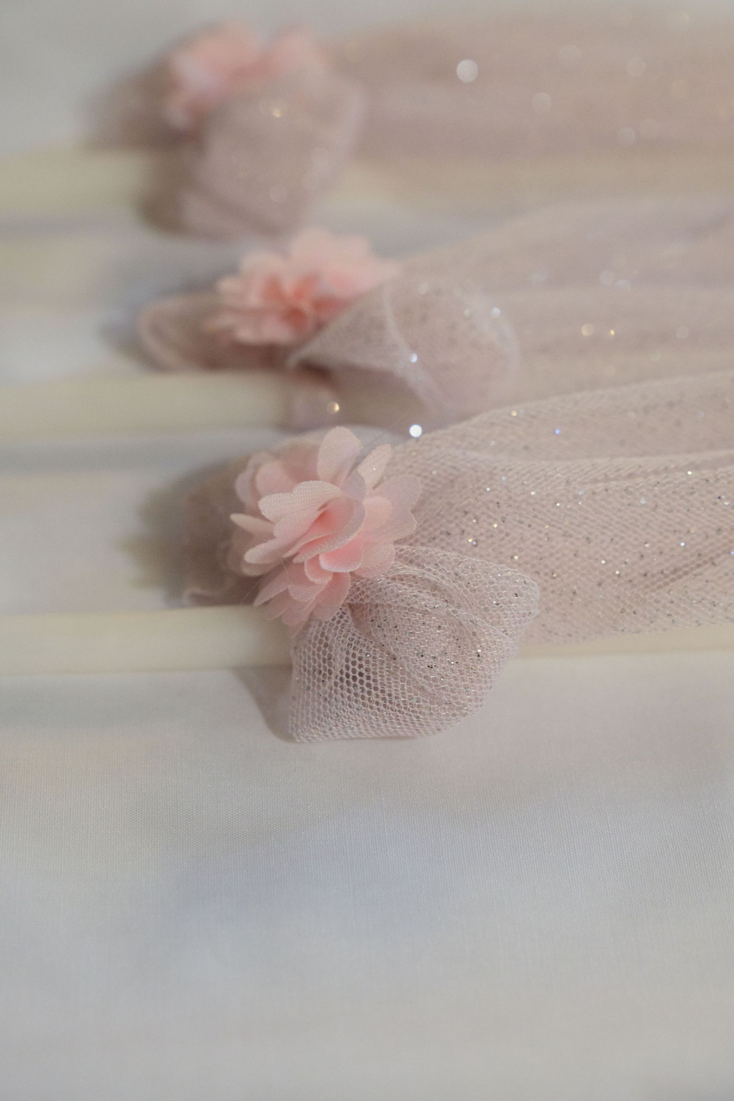 Close-up of sheer pink tulle bows with sparkly details on white surface.
