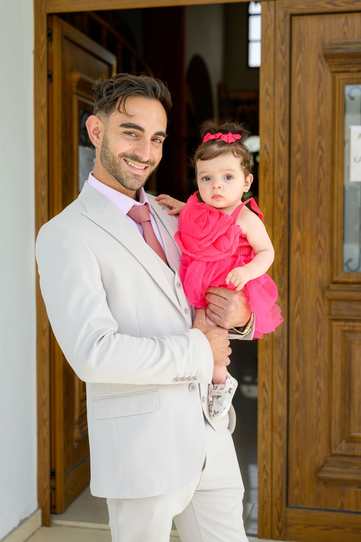 A person in light colored suit holding a small child in bright pink dress.