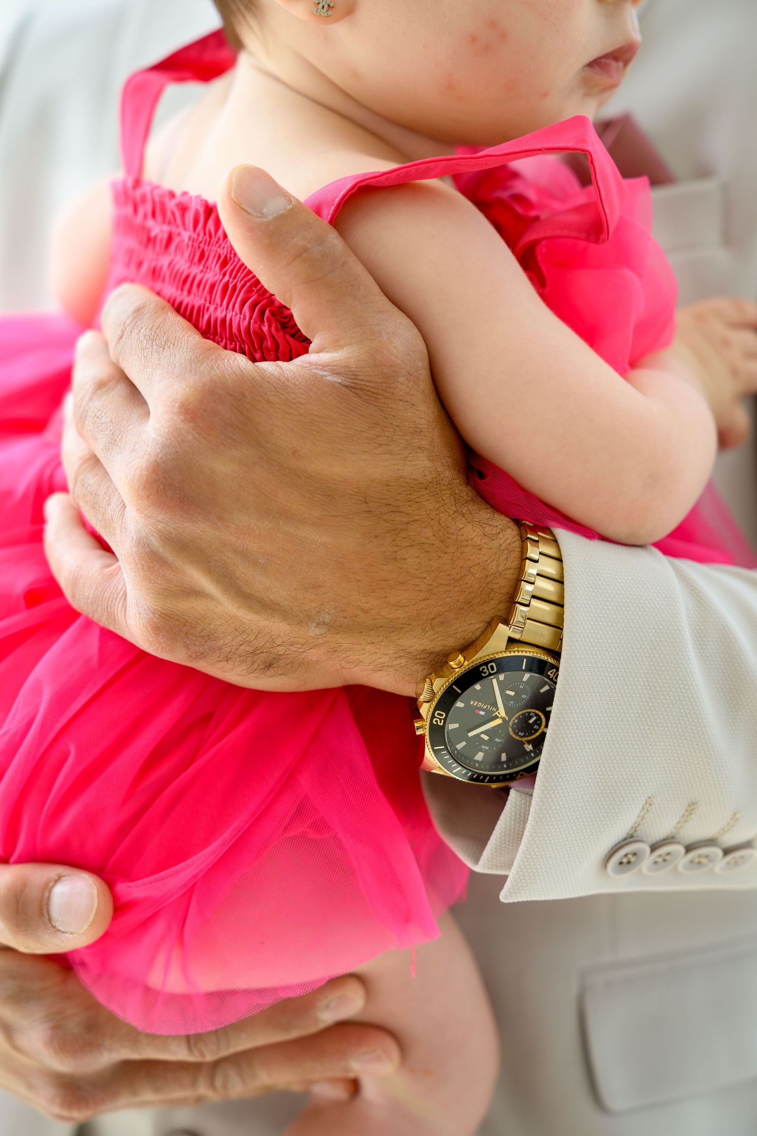 Close up of hands holding pink dress with gold watch detail.
