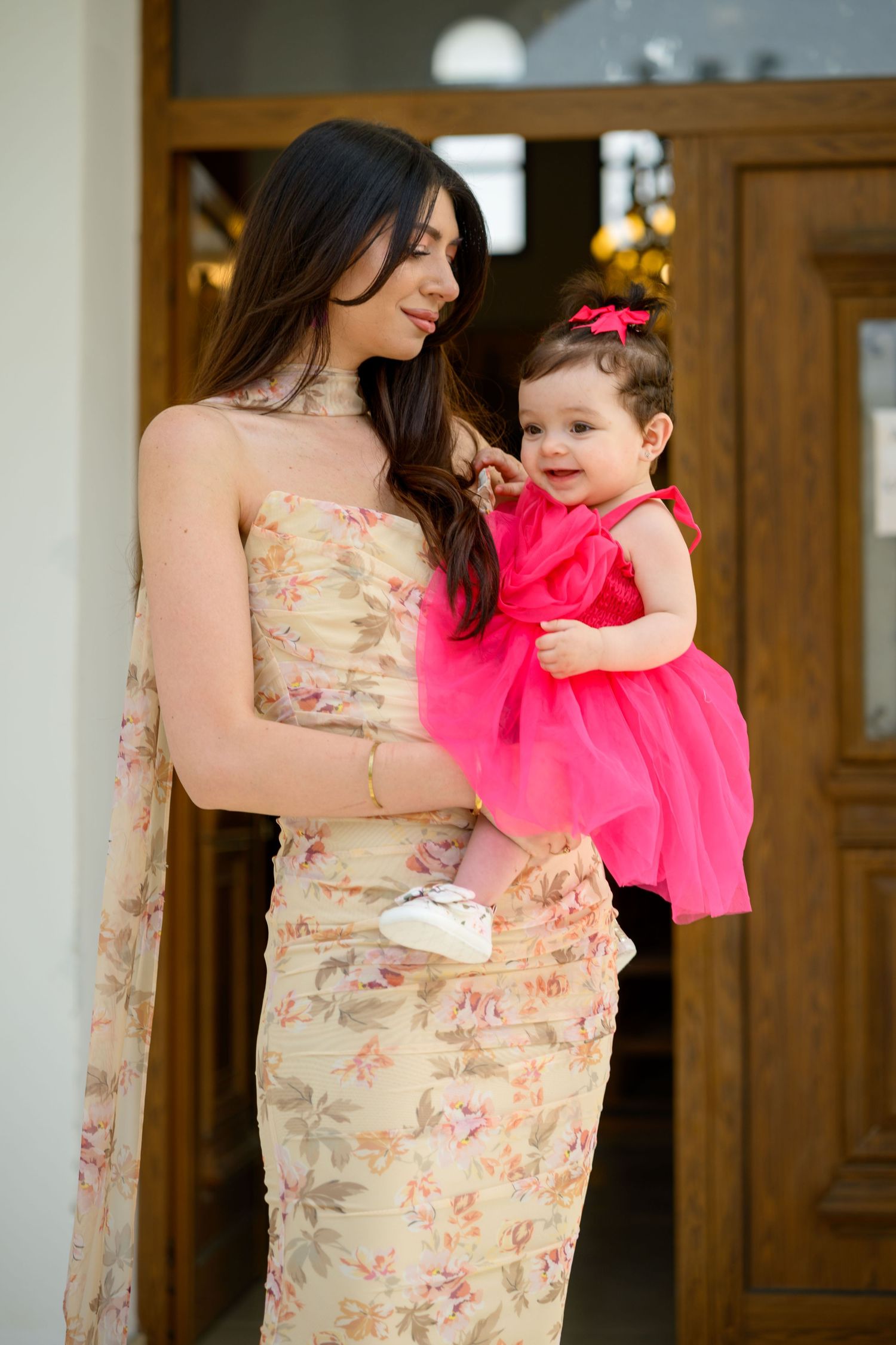 Standing figure in floral dress holding small child in bright pink party dress.