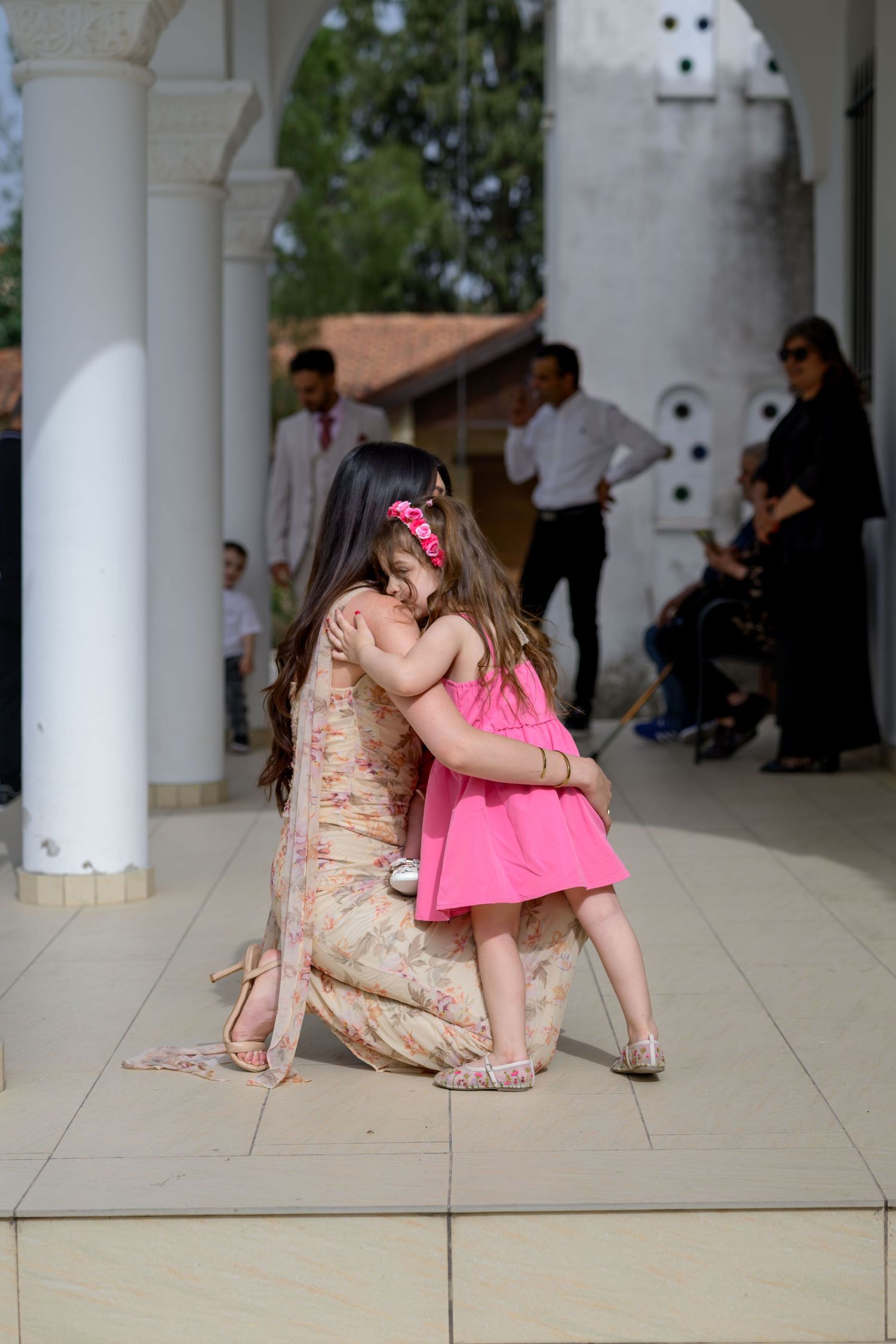 A tender moment captured between two figures in formal attire sharing an embrace on a covered patio.