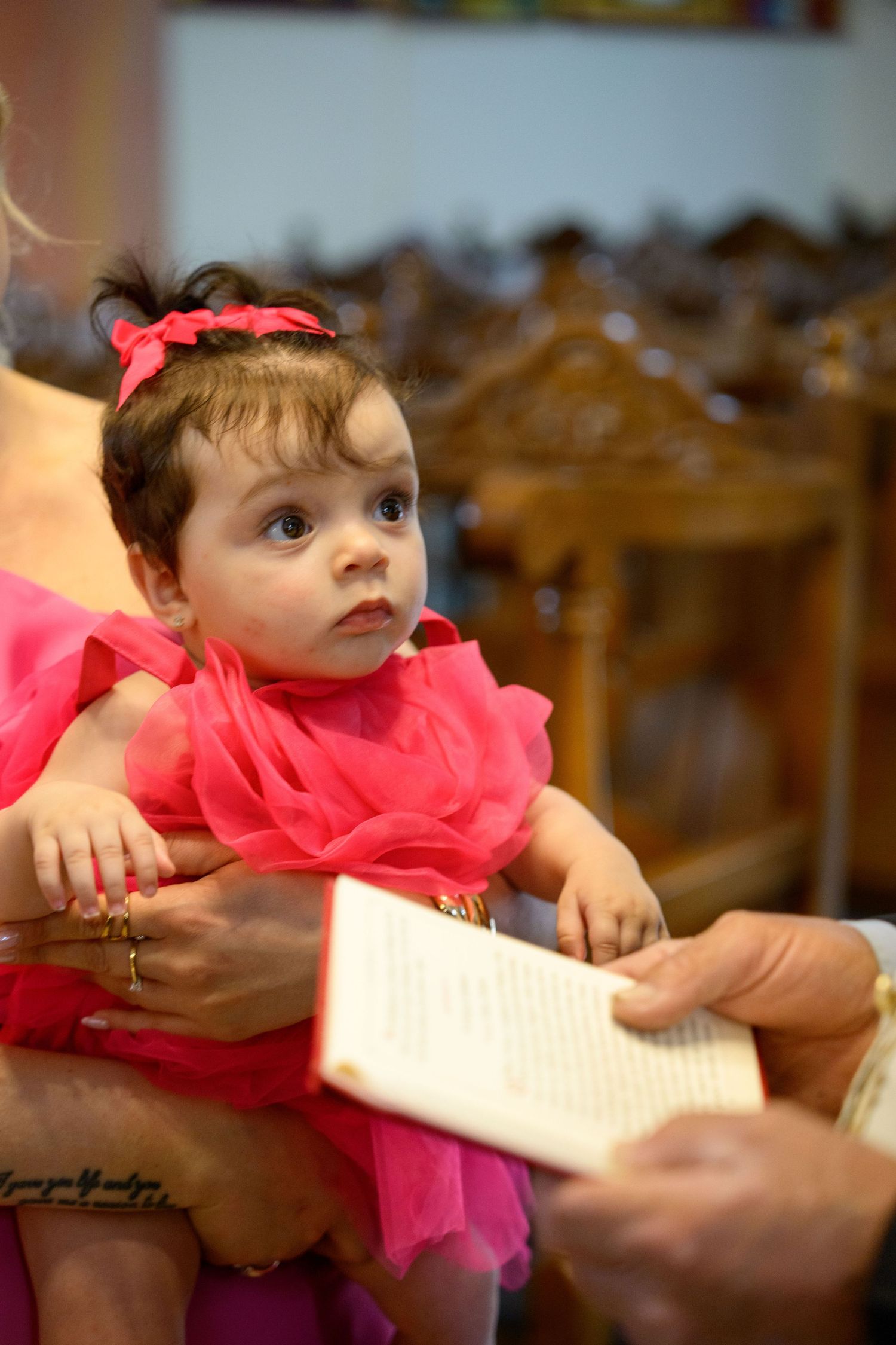 A baby in a bright pink dress during what appears to be a christening or baptism ceremony.