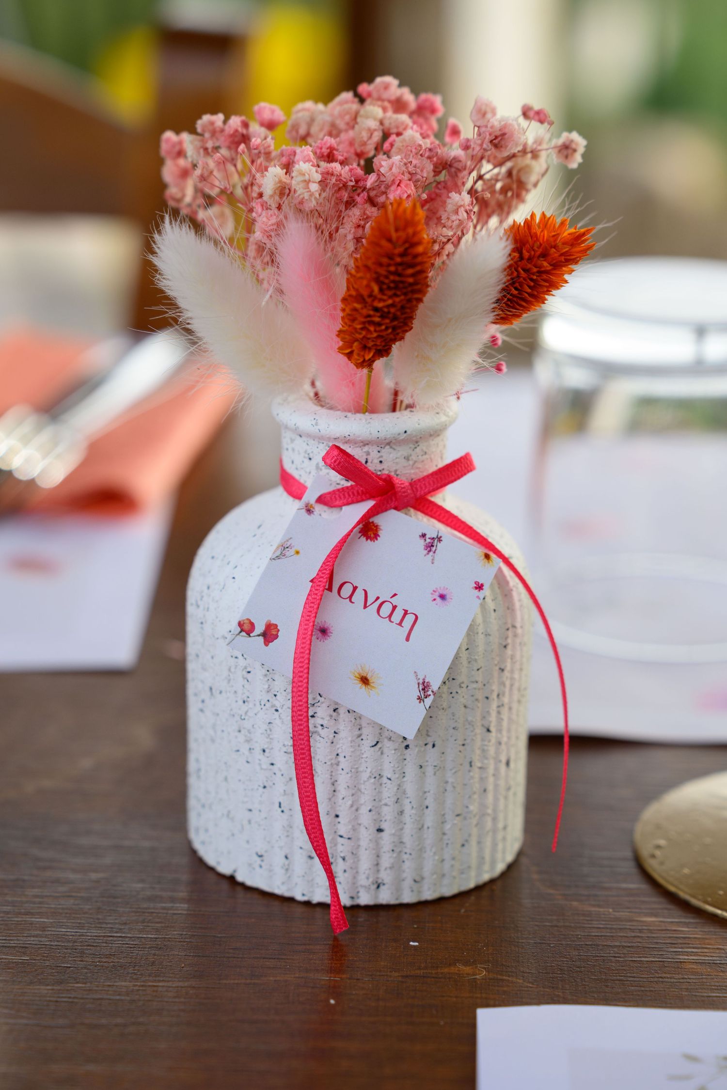 A white ceramic vase decorated with pink ribbon and dried flowers creates an elegant centerpiece.