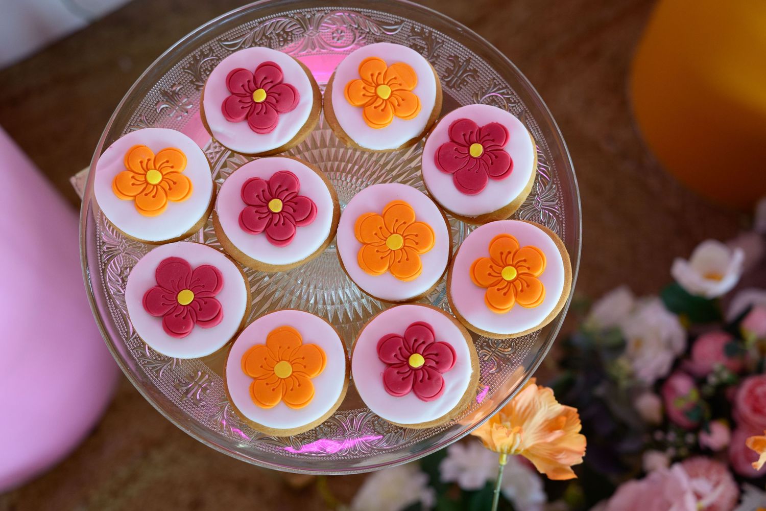 Floral-decorated sugar cookies arranged on a glass plate with pink and orange flower designs.