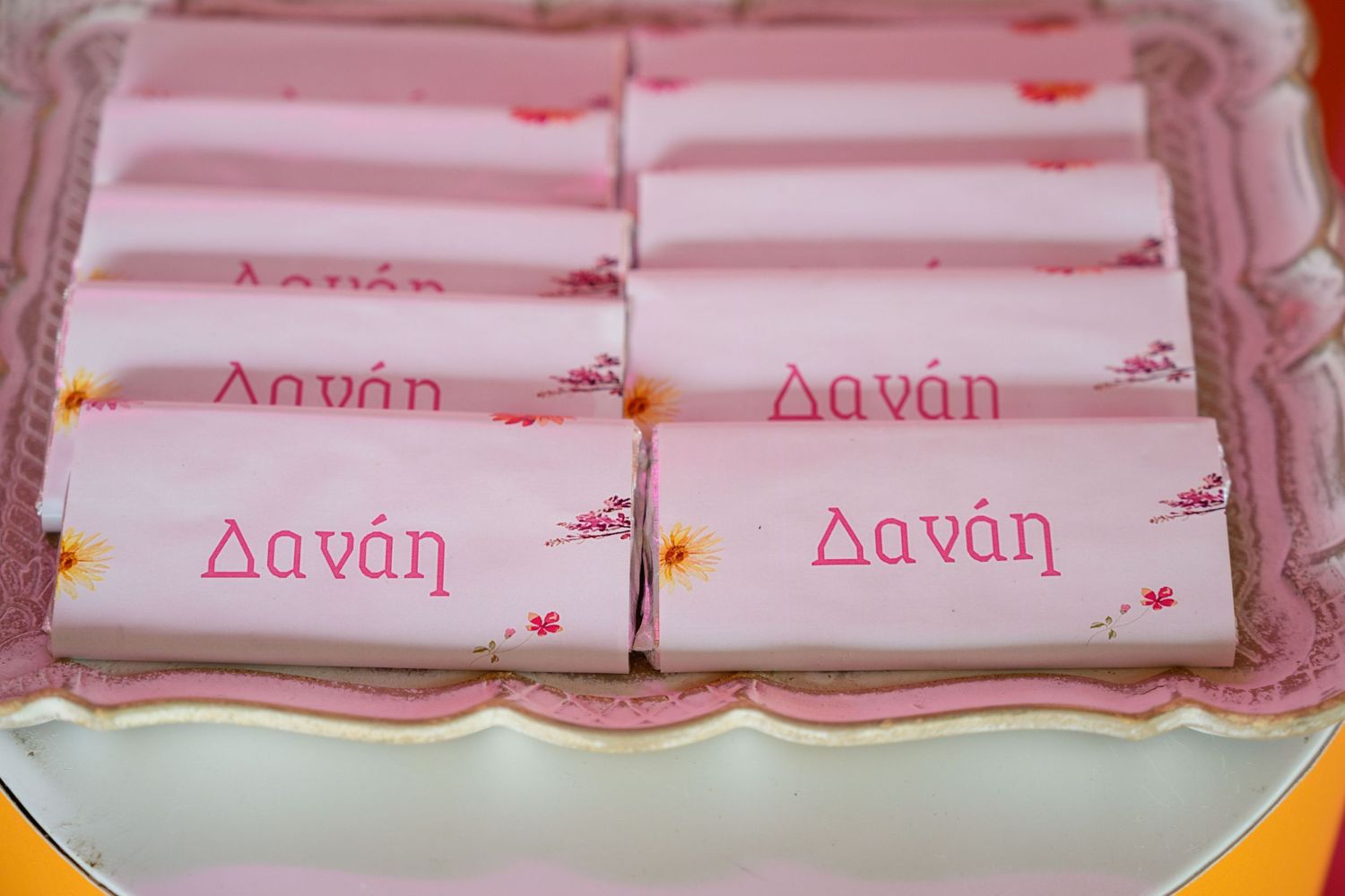 Pink-wrapped party favors with 'Danae' text written in Greek letters displayed on ornate tray.
