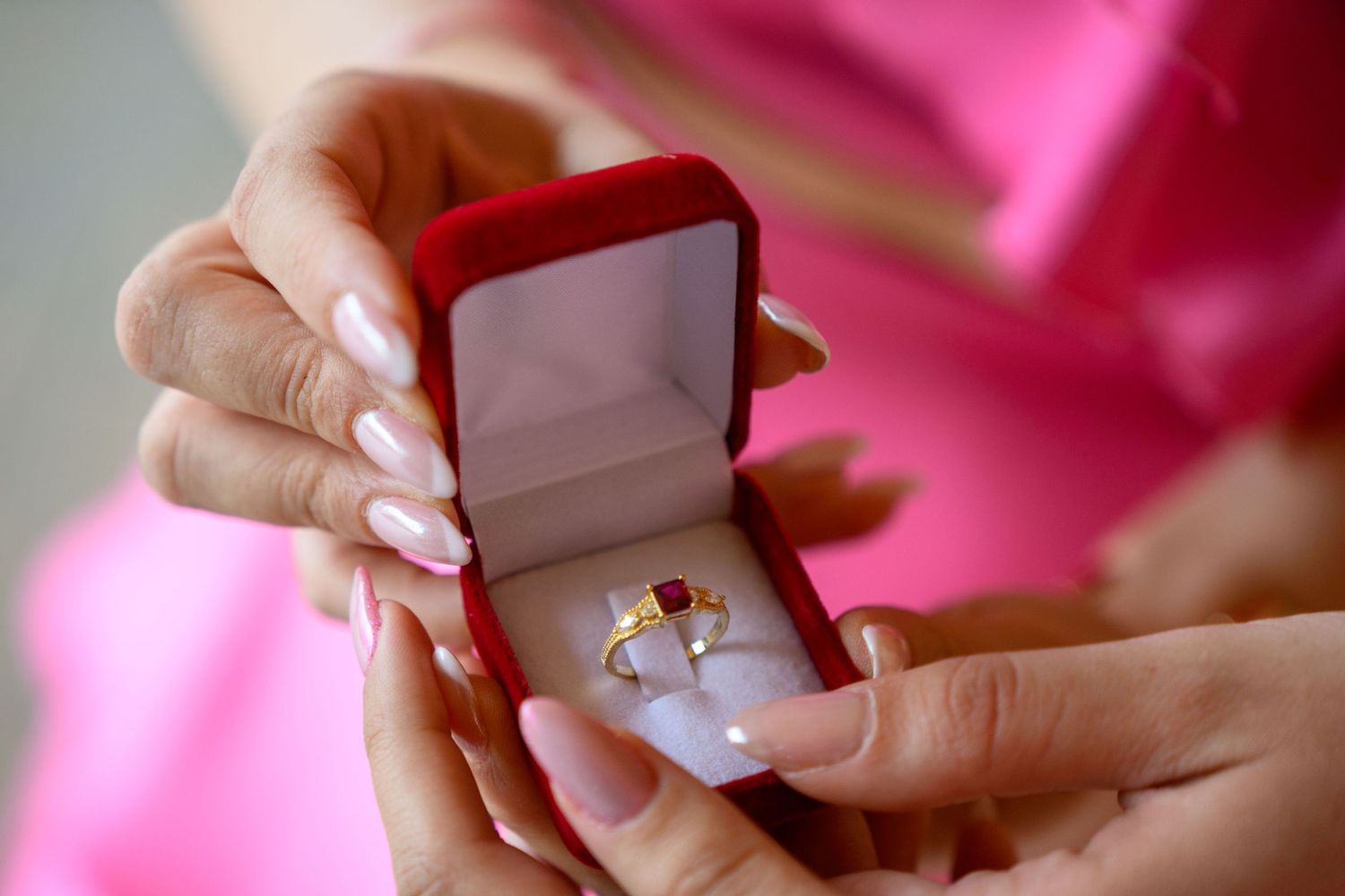 Close-up of hands holding open red ring box with engagement ring inside.