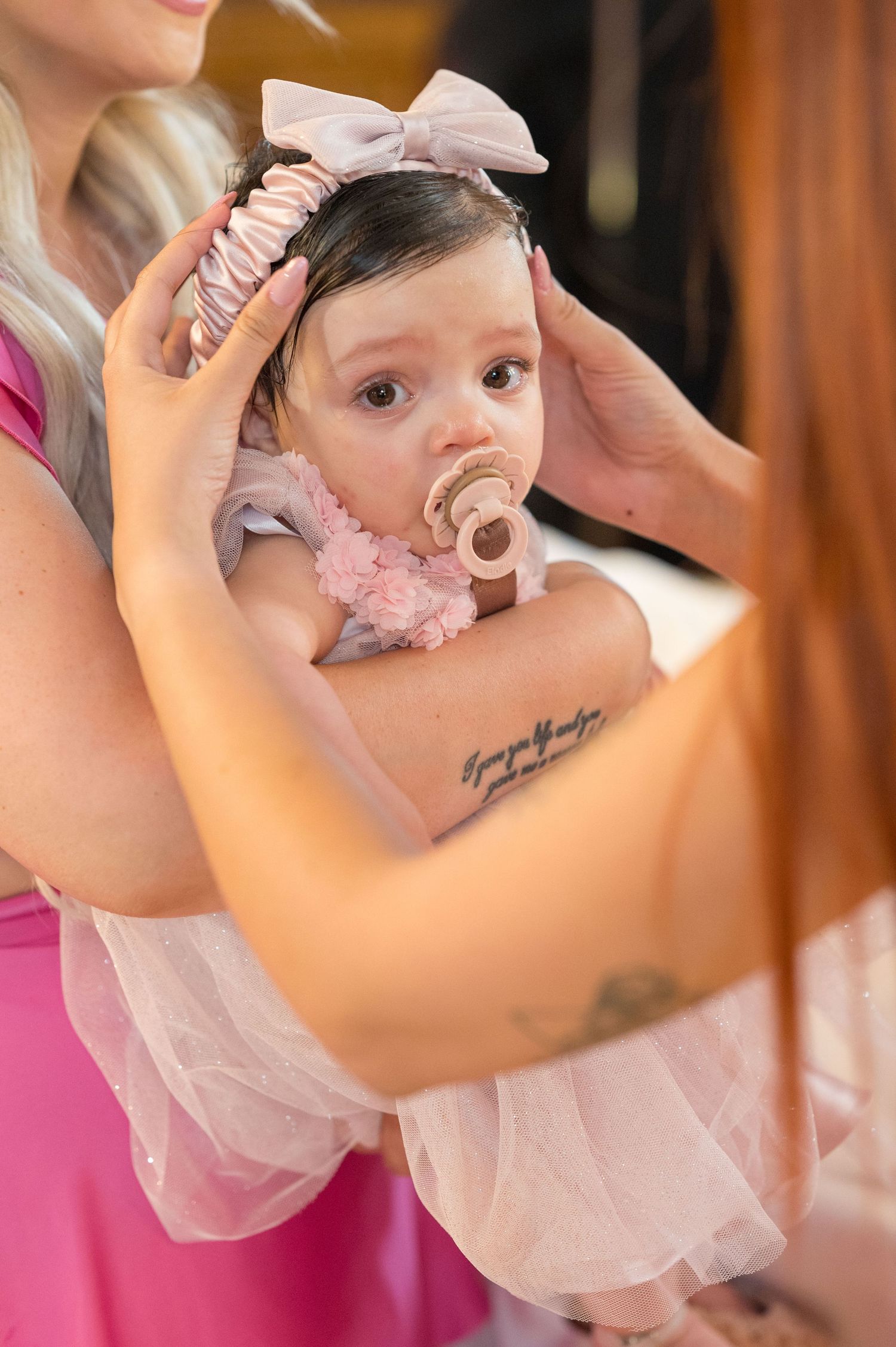 Baby in a delicate pink tulle dress being held during a special occasion.