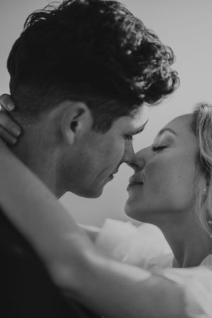 Black and white photo of bride and groom about to kiss, their noses touching and eyes closed.