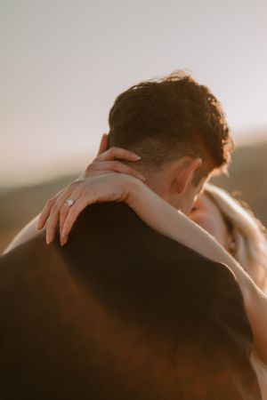 Alissa and Andrew embrace closely, focusing on Alissa's hand displaying an engagement ring.