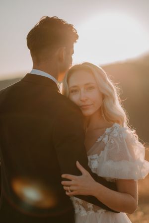 Alissa looks at the camera and embraces Andrew while he faces away, with light illuminating her face.