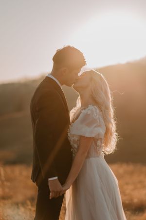 Alissa and Andrew share their first kiss at their mountain elopement in a sunlit field with a warm, glowing backdrop.