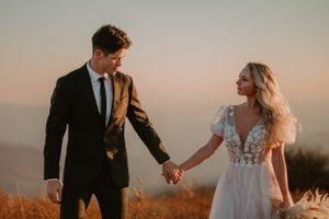 Alissa and Andrew hold hands and smile at each other as they walk along a grassy path after their elopement ceremony.